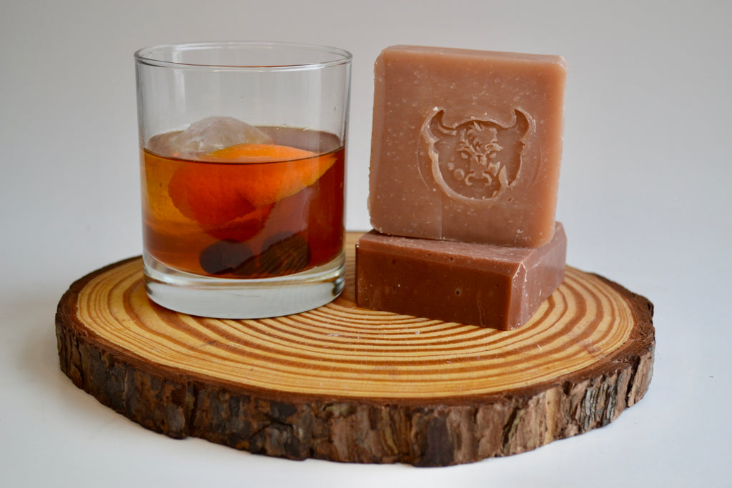Two bars of soap and a glass with an orange peel on a wooden coaster.