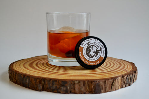 Glass of amber liquid with a round coaster featuring a logo on a wooden coaster.