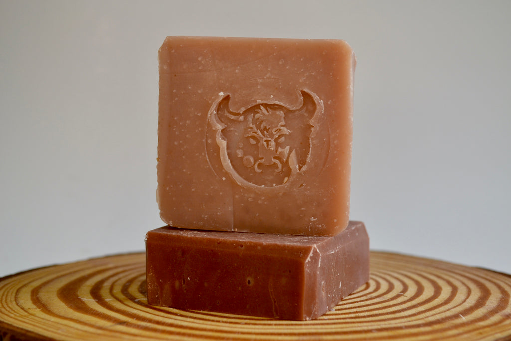 Two brown soap bars with a bull logo on a wooden surface