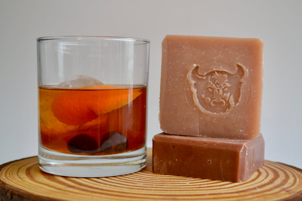 Two bars of soap and a glass of iced tea on a wooden surface with a plain background