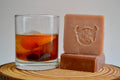 Two bars of soap and a glass of iced tea on a wooden surface with a plain background