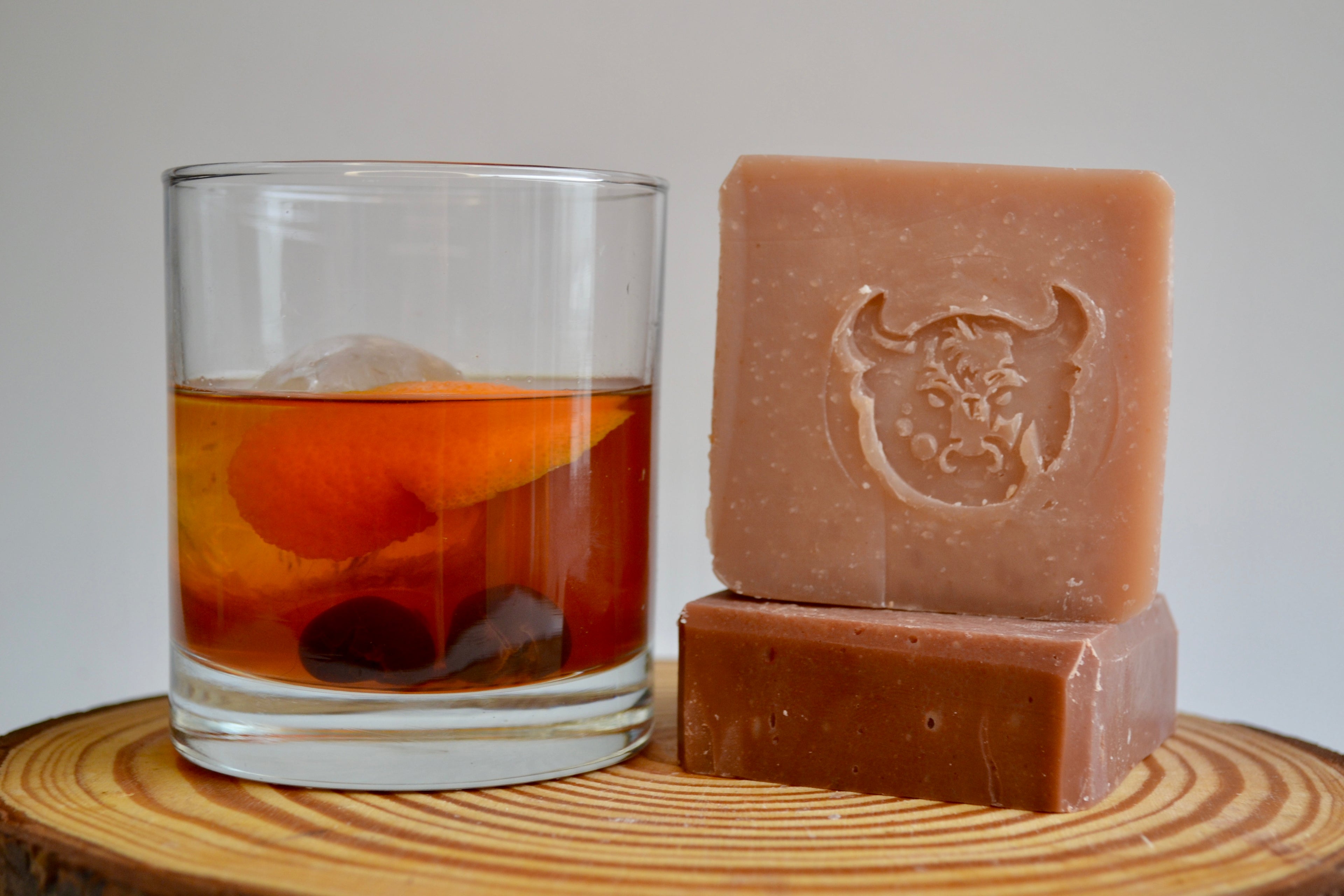 Two bars of soap and a glass of iced tea on a wooden surface with a plain background