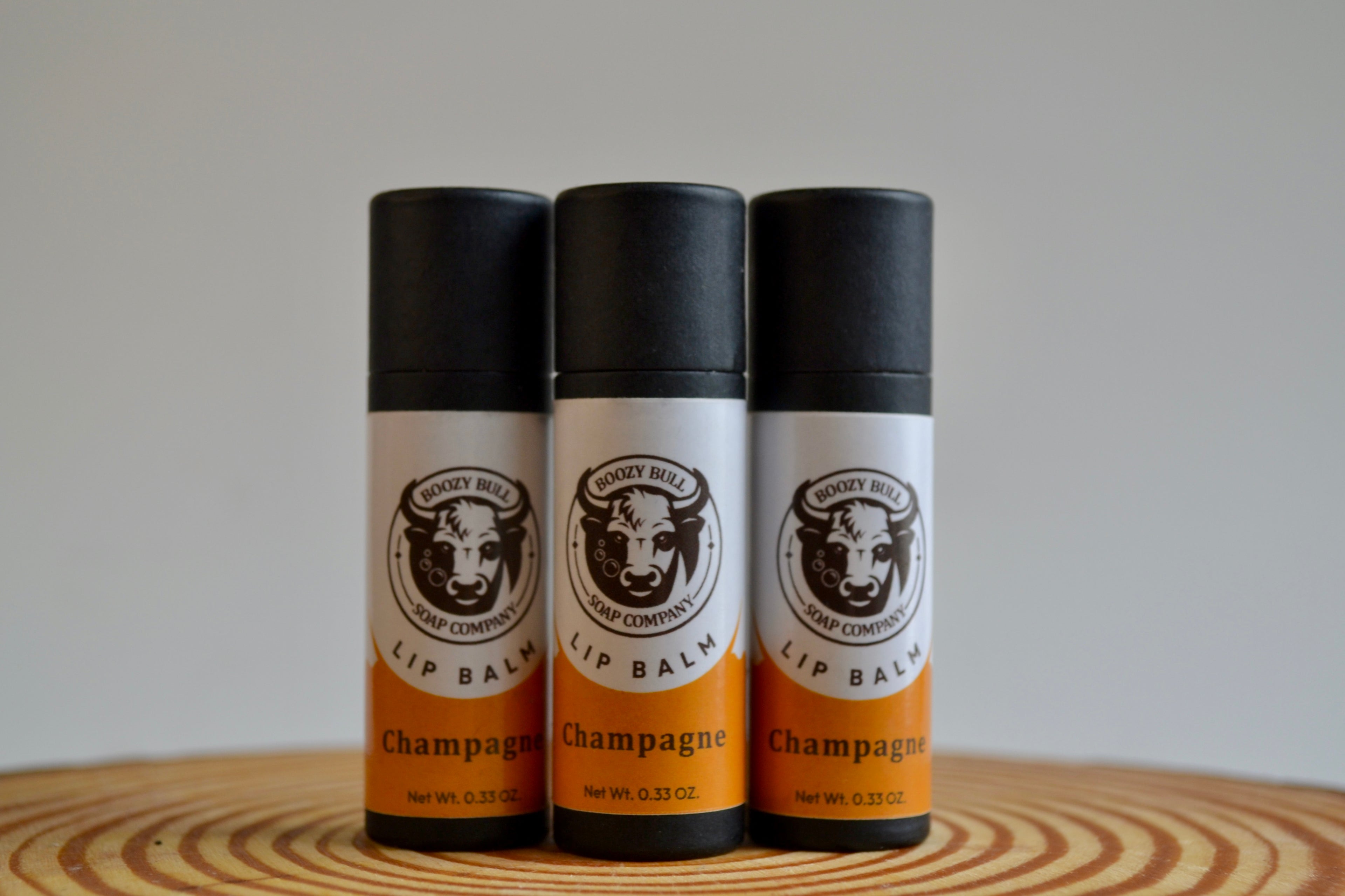 Three lip balm tubes labeled 'Champagne' on a wooden surface with a neutral background