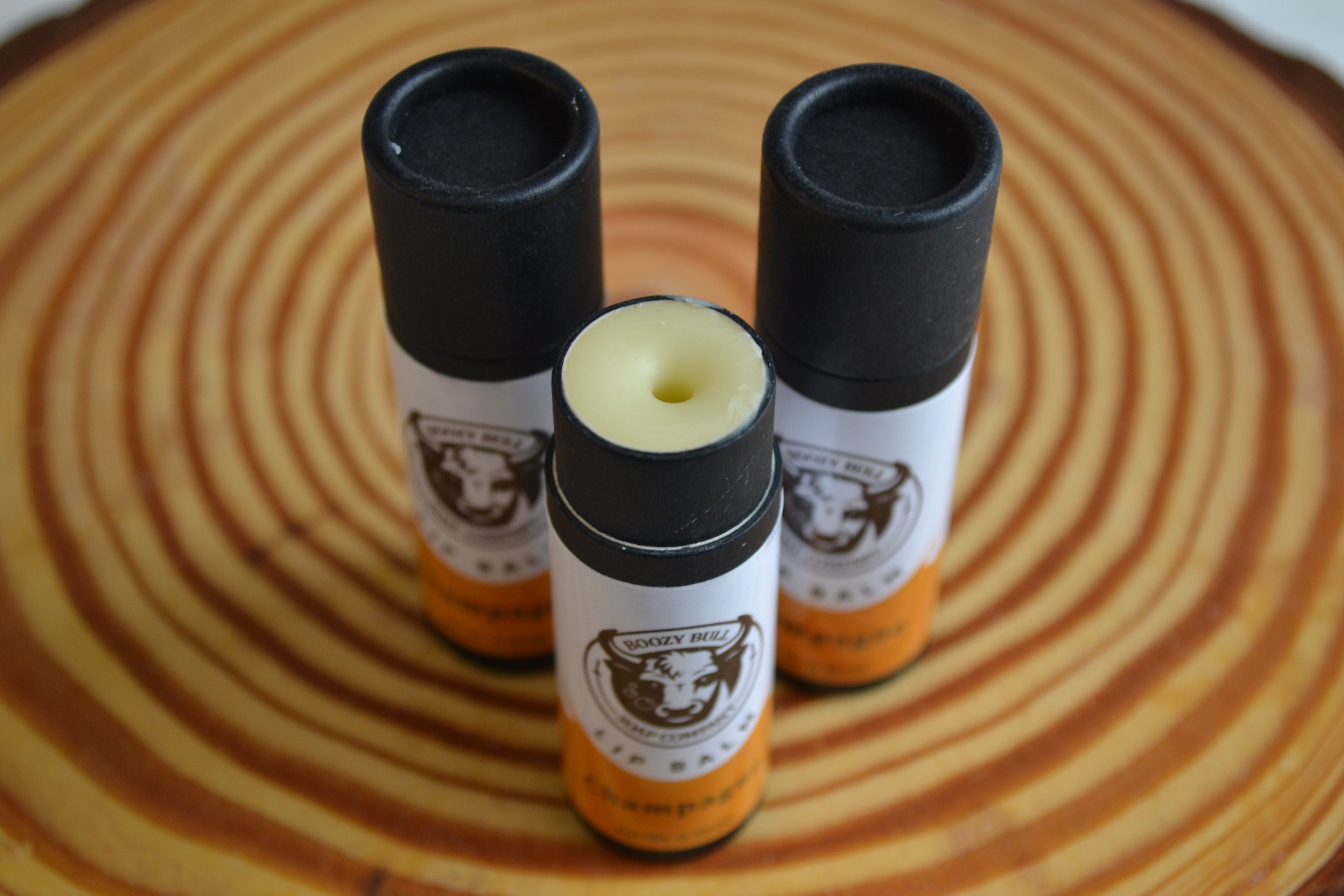Three lip balm tubes with black caps on a wooden surface