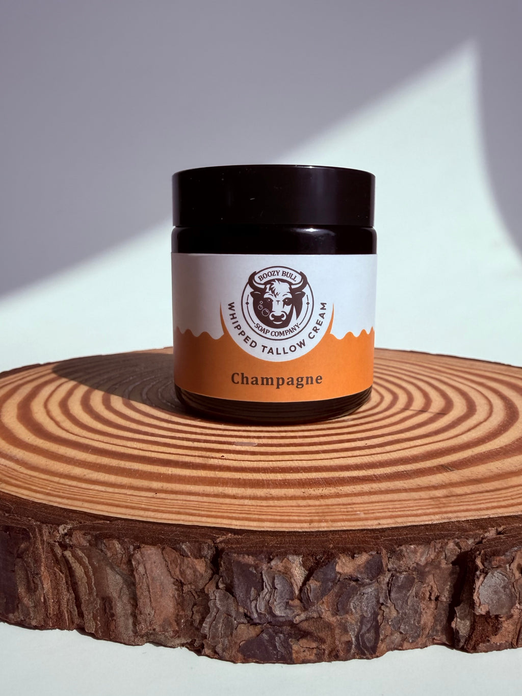 Jar of whipped tallow cream labeled 'Champagne' on a wooden surface with a white background