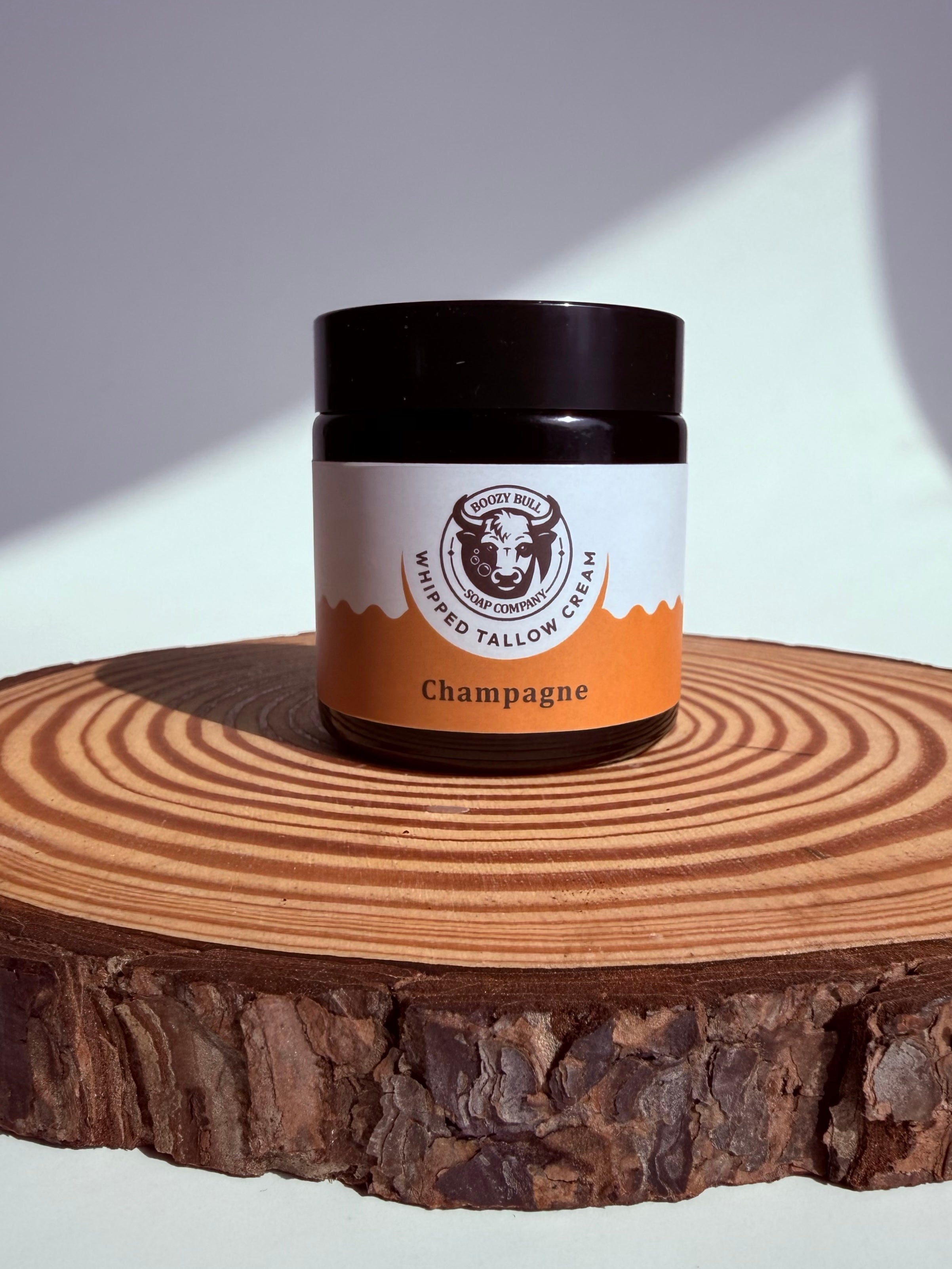 Jar of whipped tallow cream labeled 'Champagne' on a wooden surface with a white background
