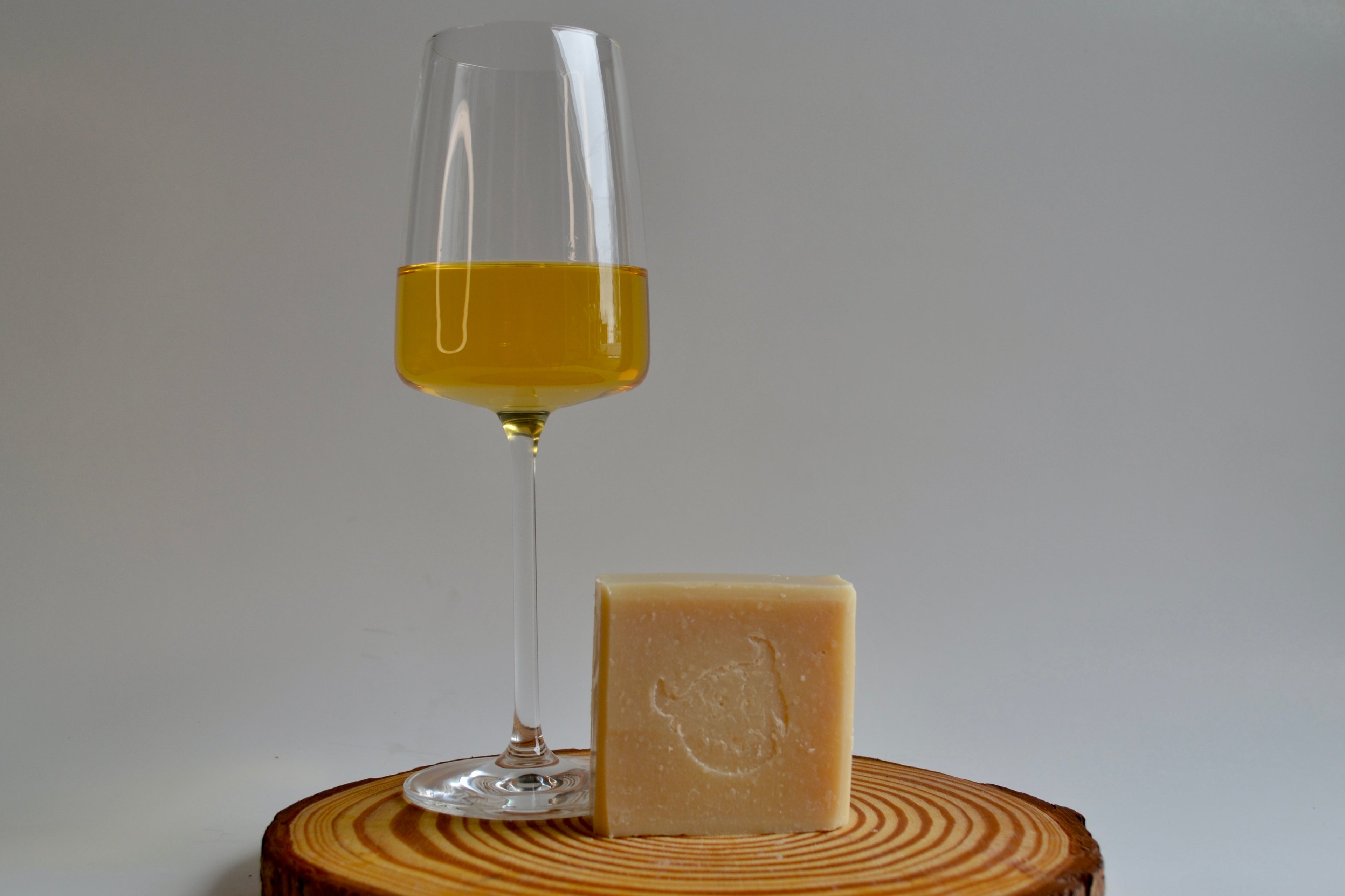 Glass of yellow liquid next to a bar of soap on a wooden surface with a white background