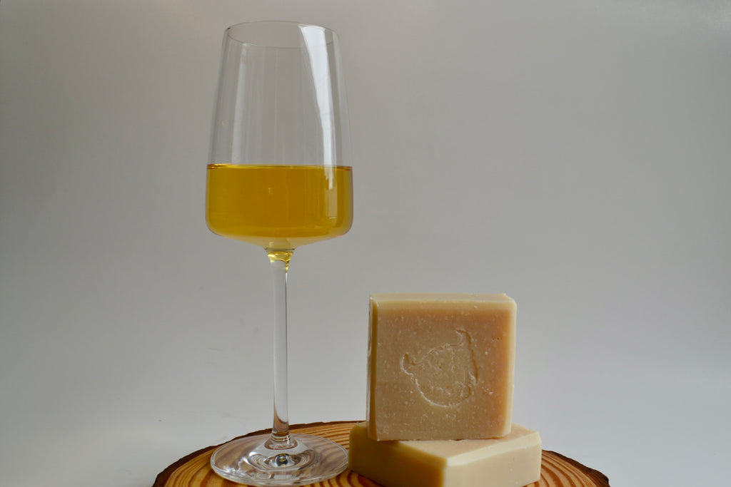 Glass of yellow liquid next to two bars of soap on a wooden board with a gray background