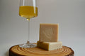 Two bars of soap on a wooden surface next to a glass of yellow liquid.