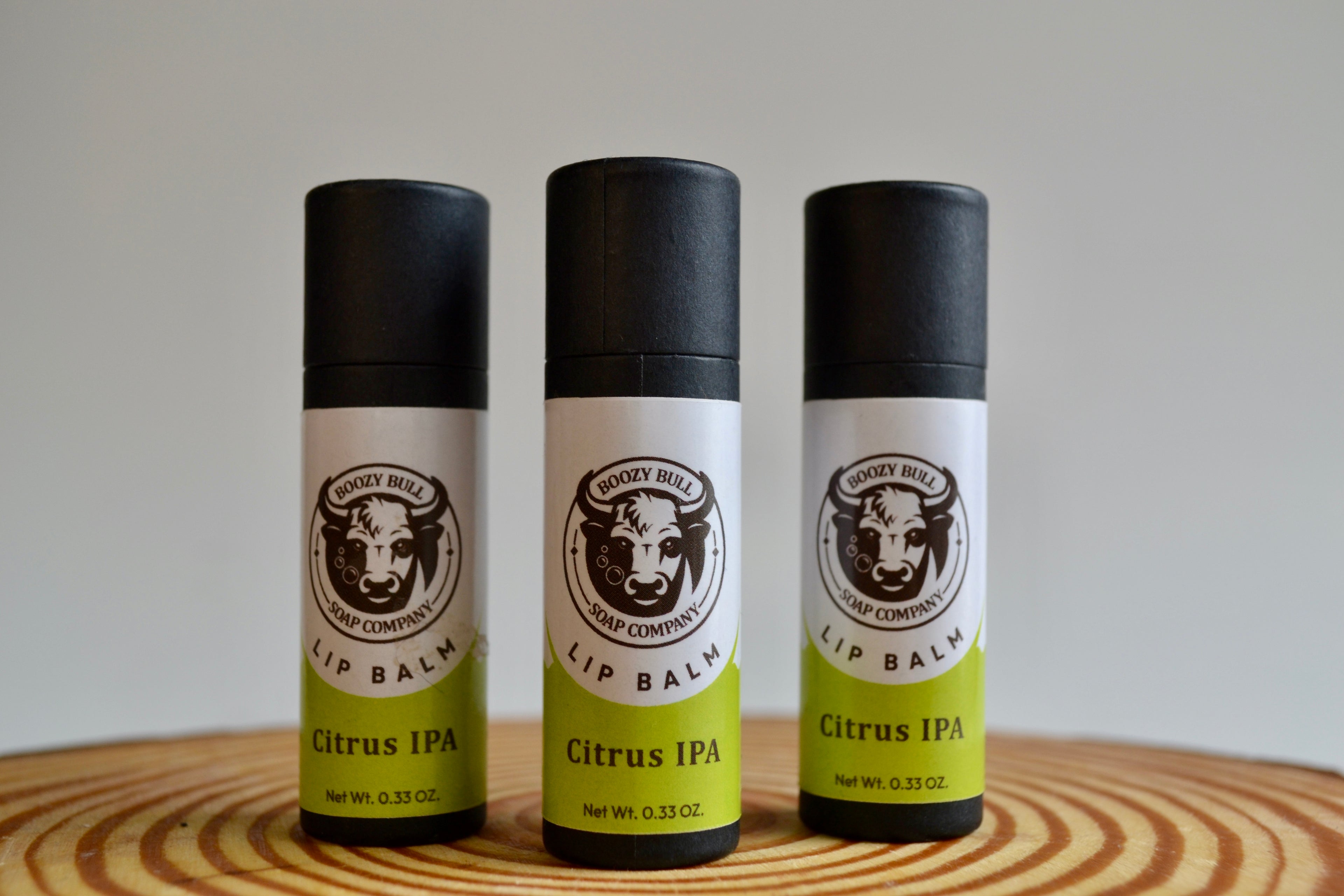 Three lip balm containers with 'Citrus IPA' flavor on a wooden surface.