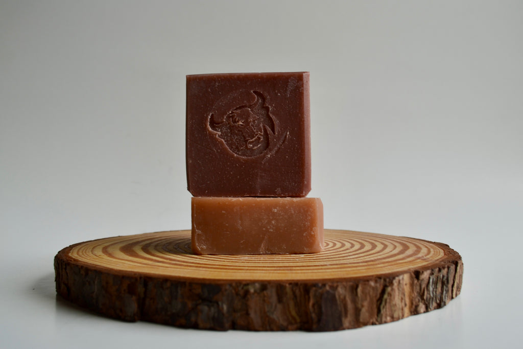 Two bars of brown soap stacked on a wooden disc with a plain background