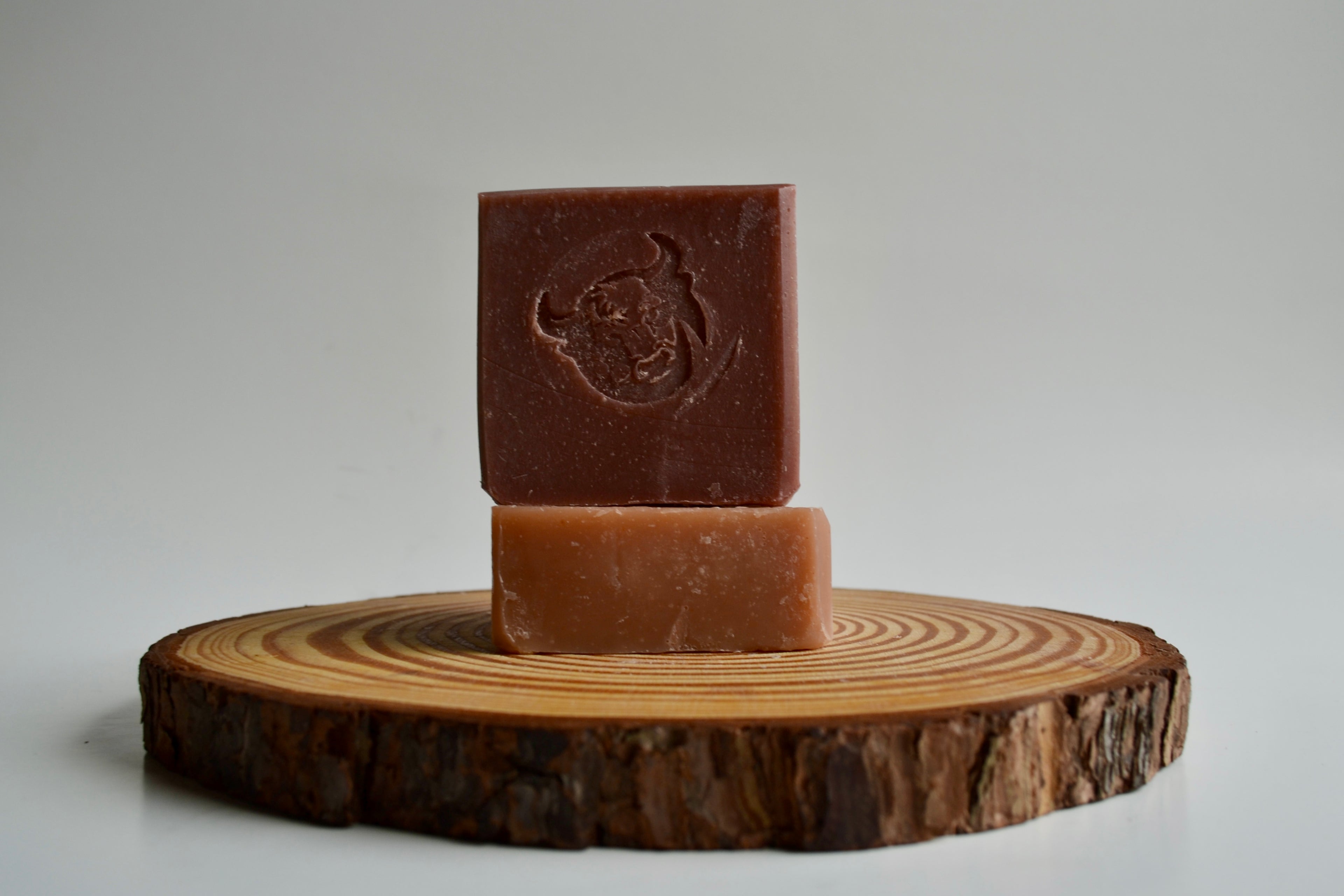 Two bars of brown soap stacked on a wooden disc with a plain background