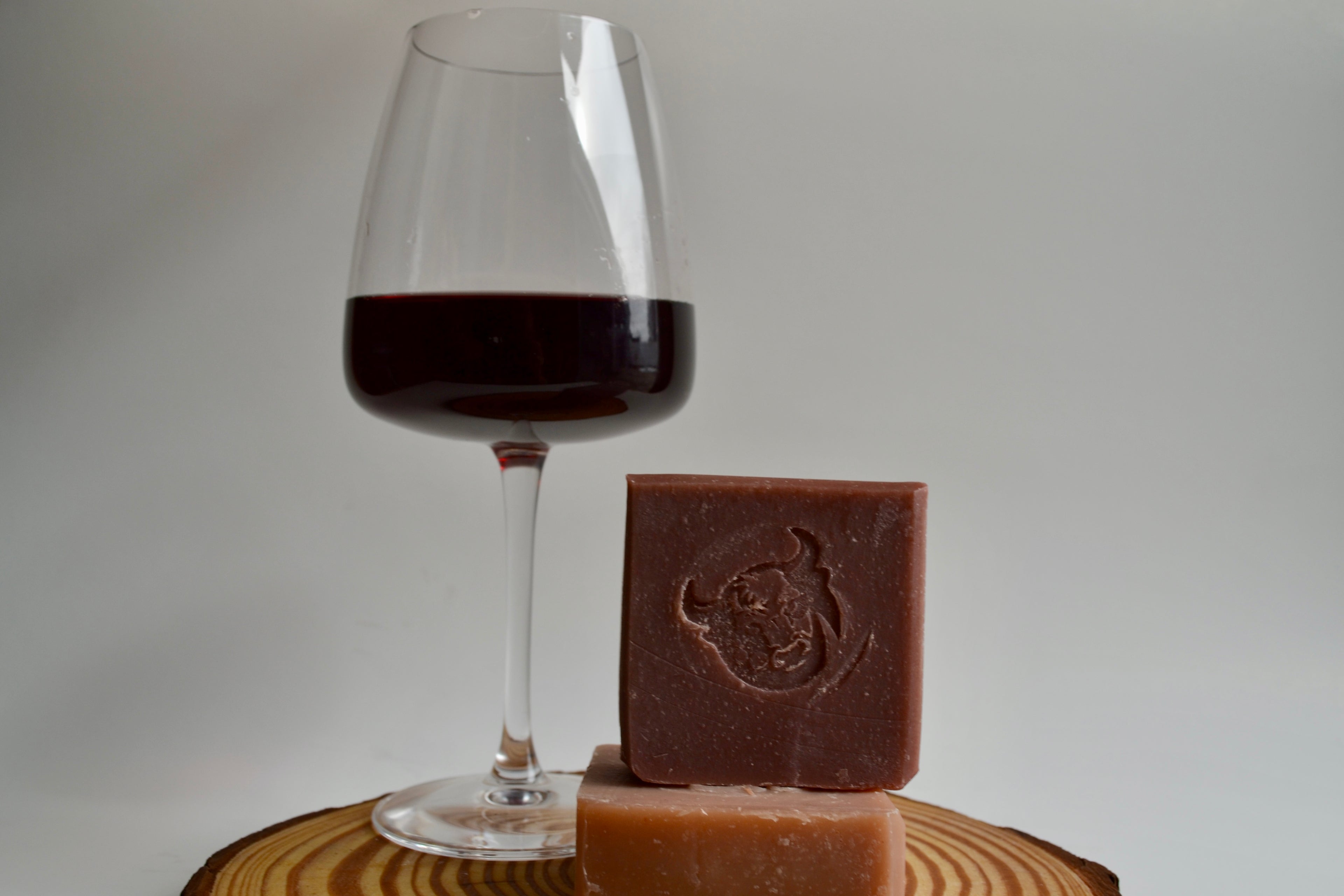 Bar of chocolate soap next to a glass of red wine on a wooden surface.