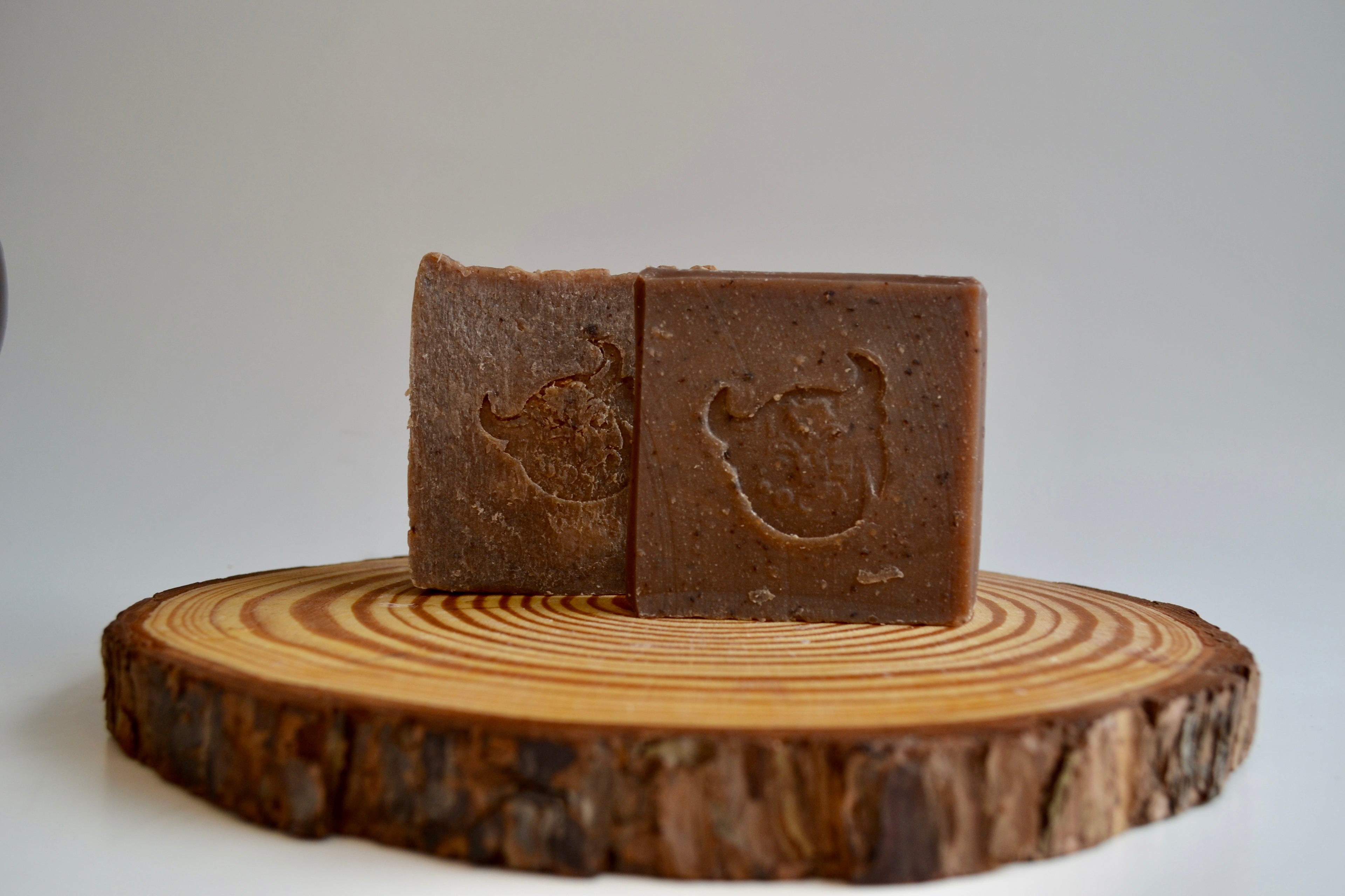 Two brown soap bars with a logo on a wooden stand against a white background
