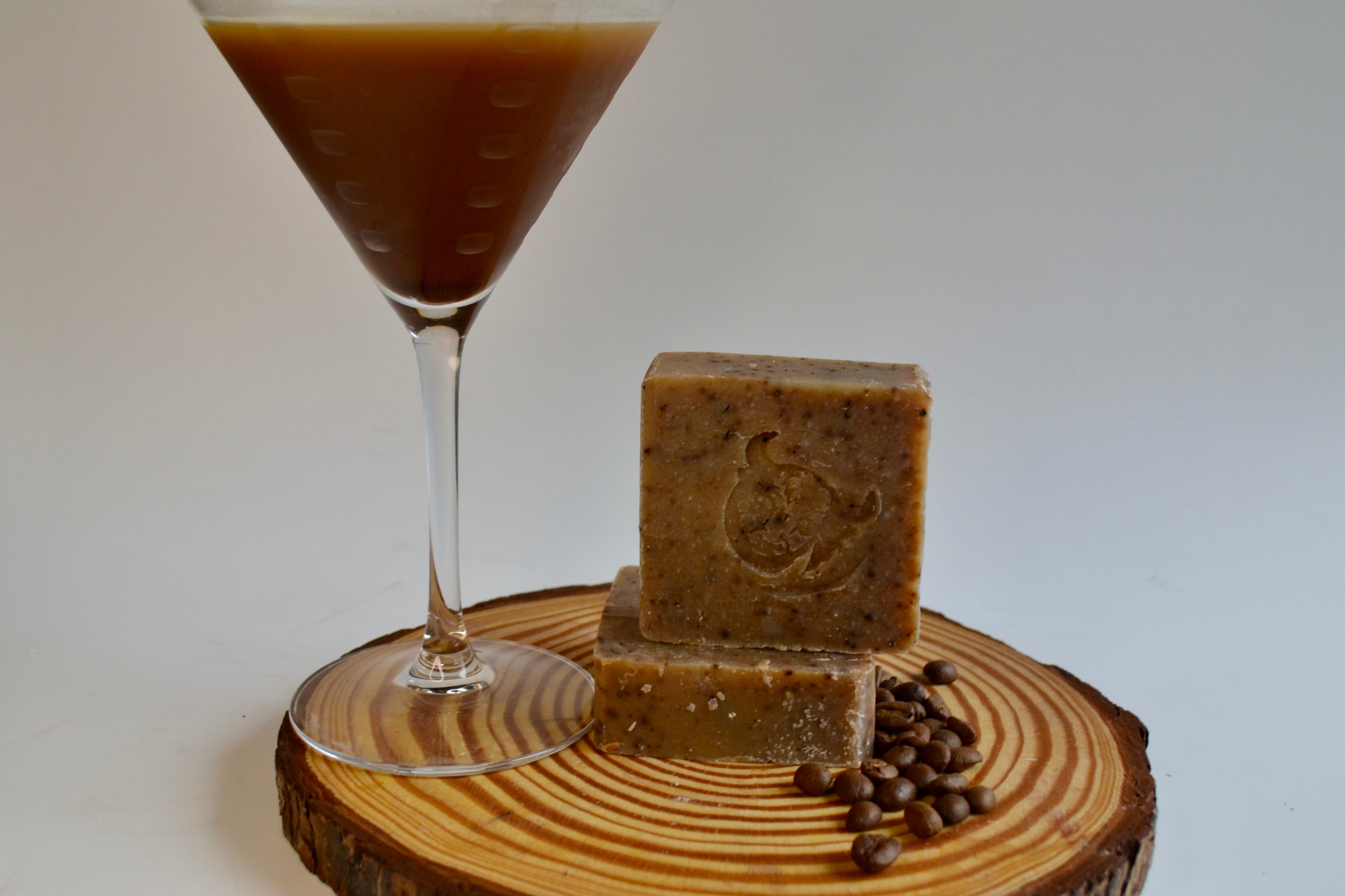 Two blocks of soap and a glass of coffee on a wooden coaster with coffee beans.