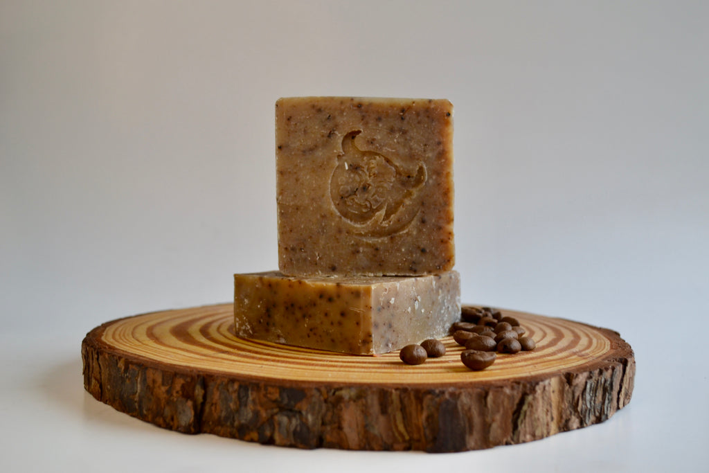 Three bars of soap on a wooden platter with coffee beans on a white background