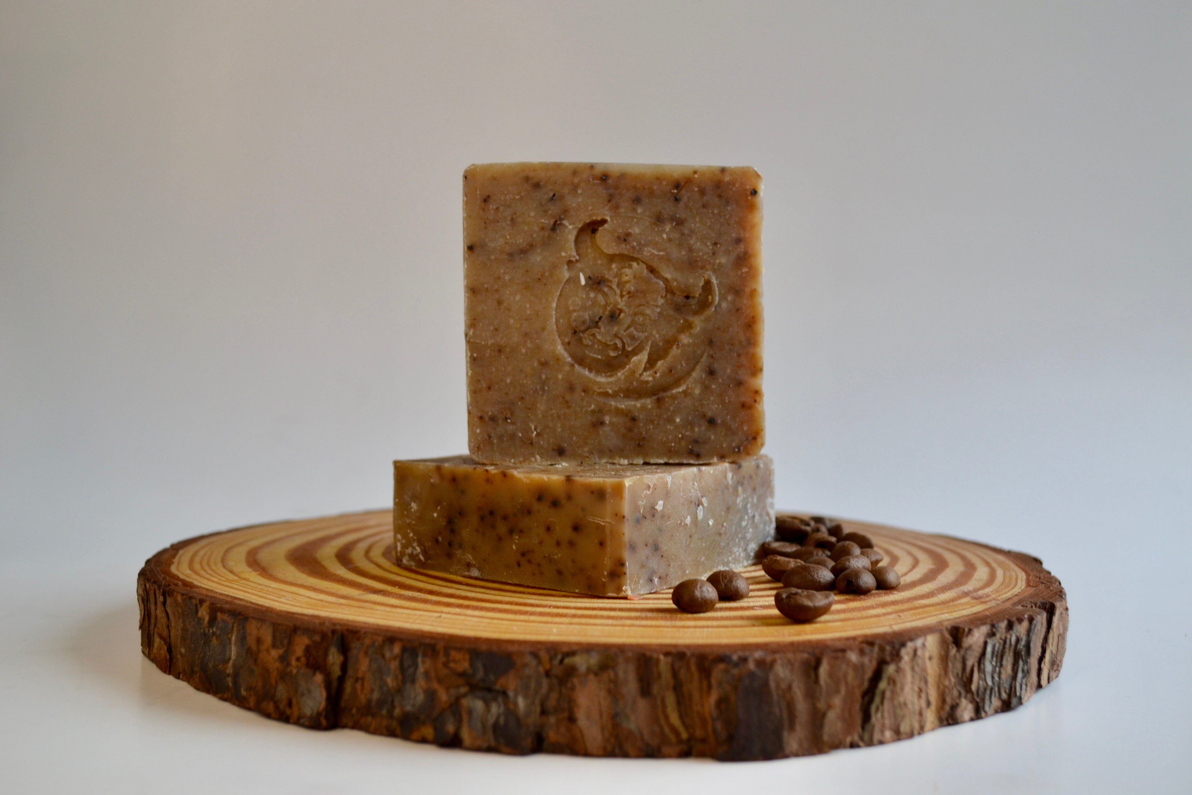 Three bars of soap on a wooden platter with coffee beans on a white background