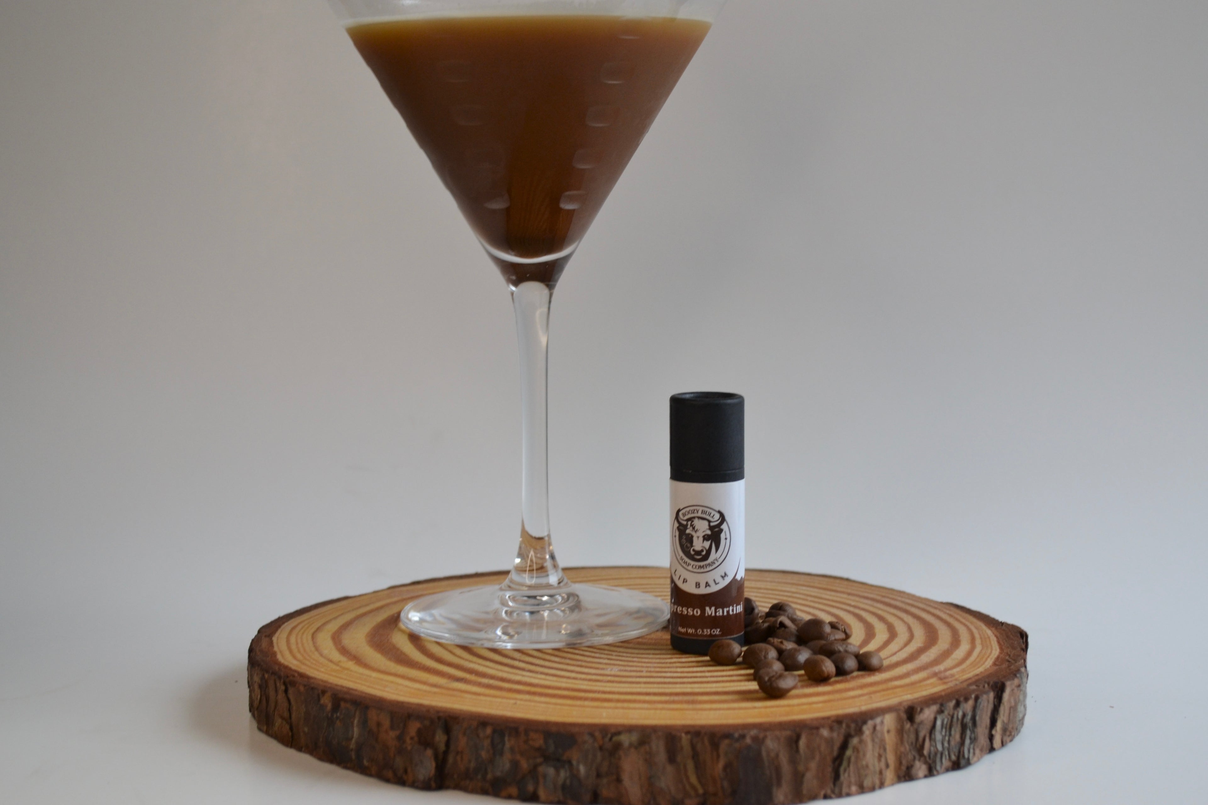 Cocktail in a martini glass with coffee beans and a bottle on a wooden coaster.