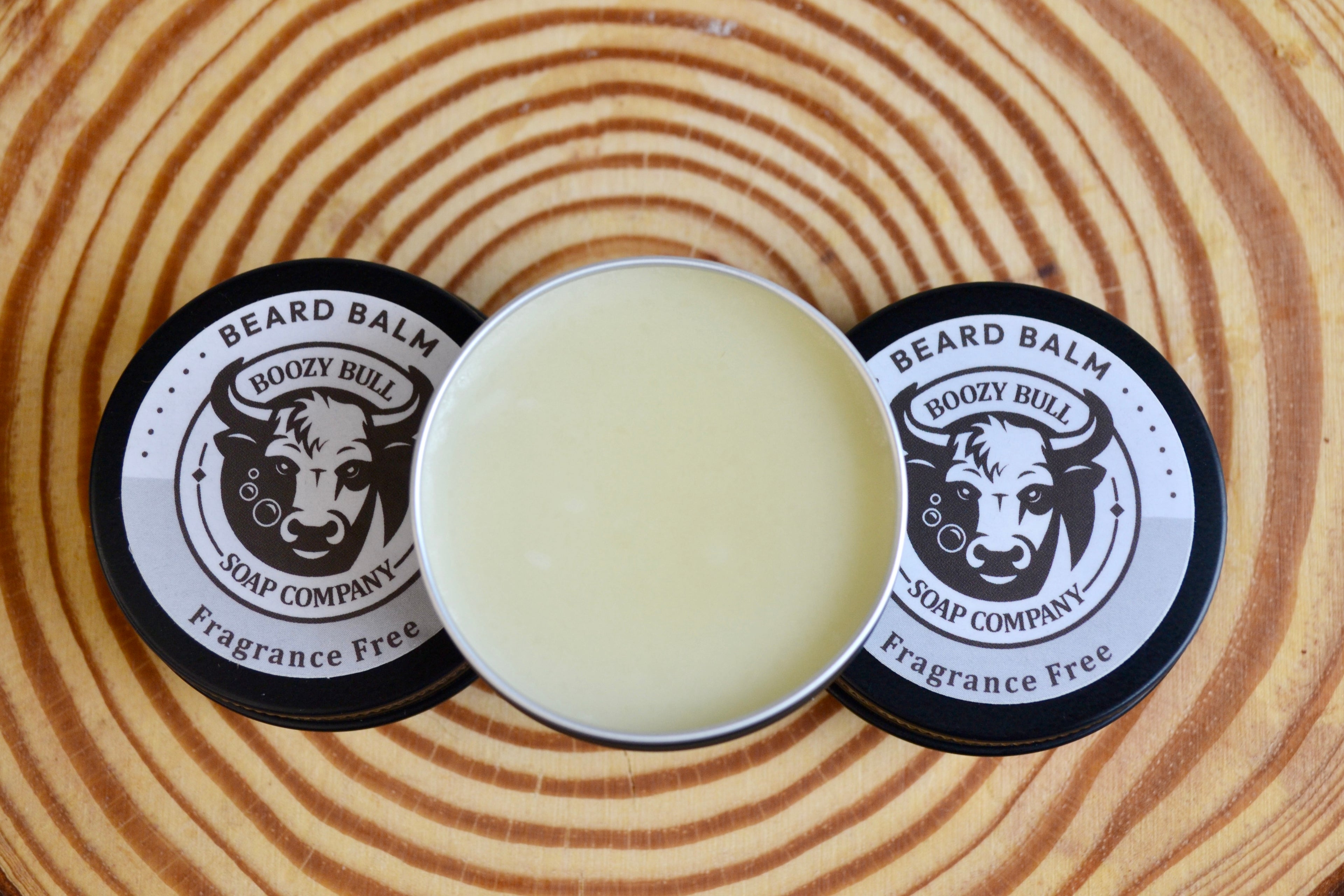 Beard balm container with lid on a wooden surface, featuring 'Boozy Bull Soap Company' branding.