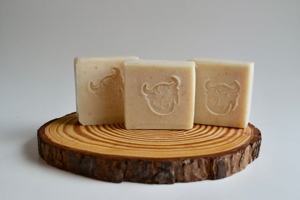 Three bars of soap with a bull logo on a wooden block against a white background