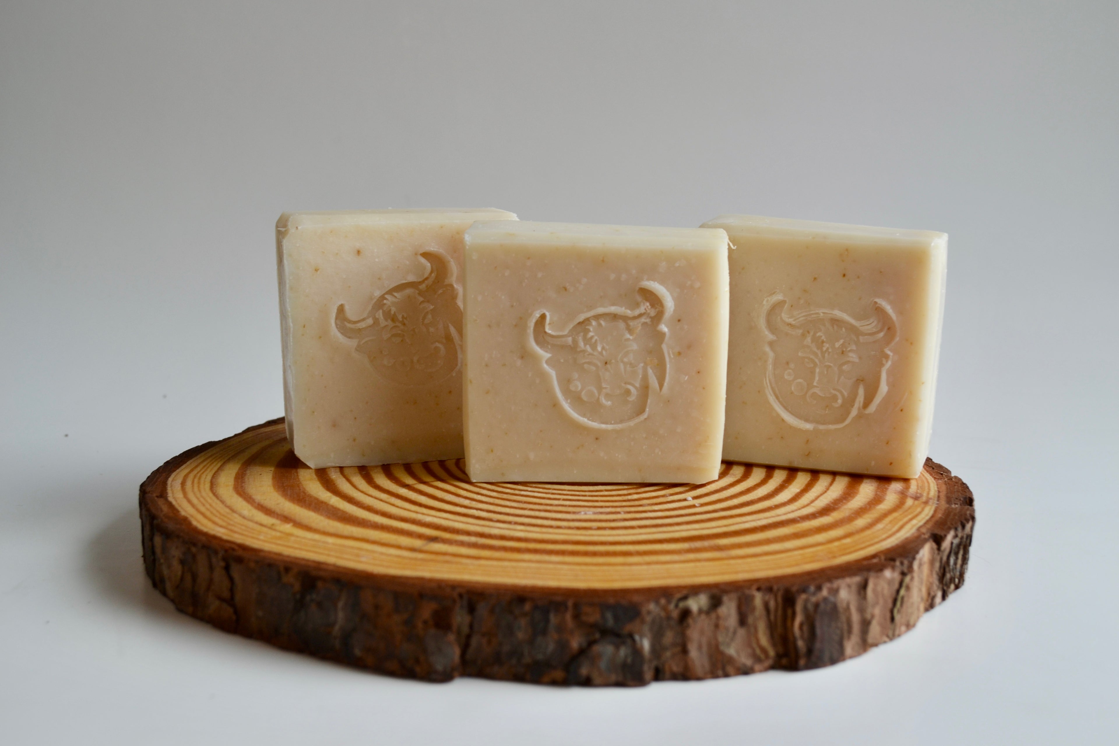 Three bars of soap with a bull logo on a wooden block against a white background