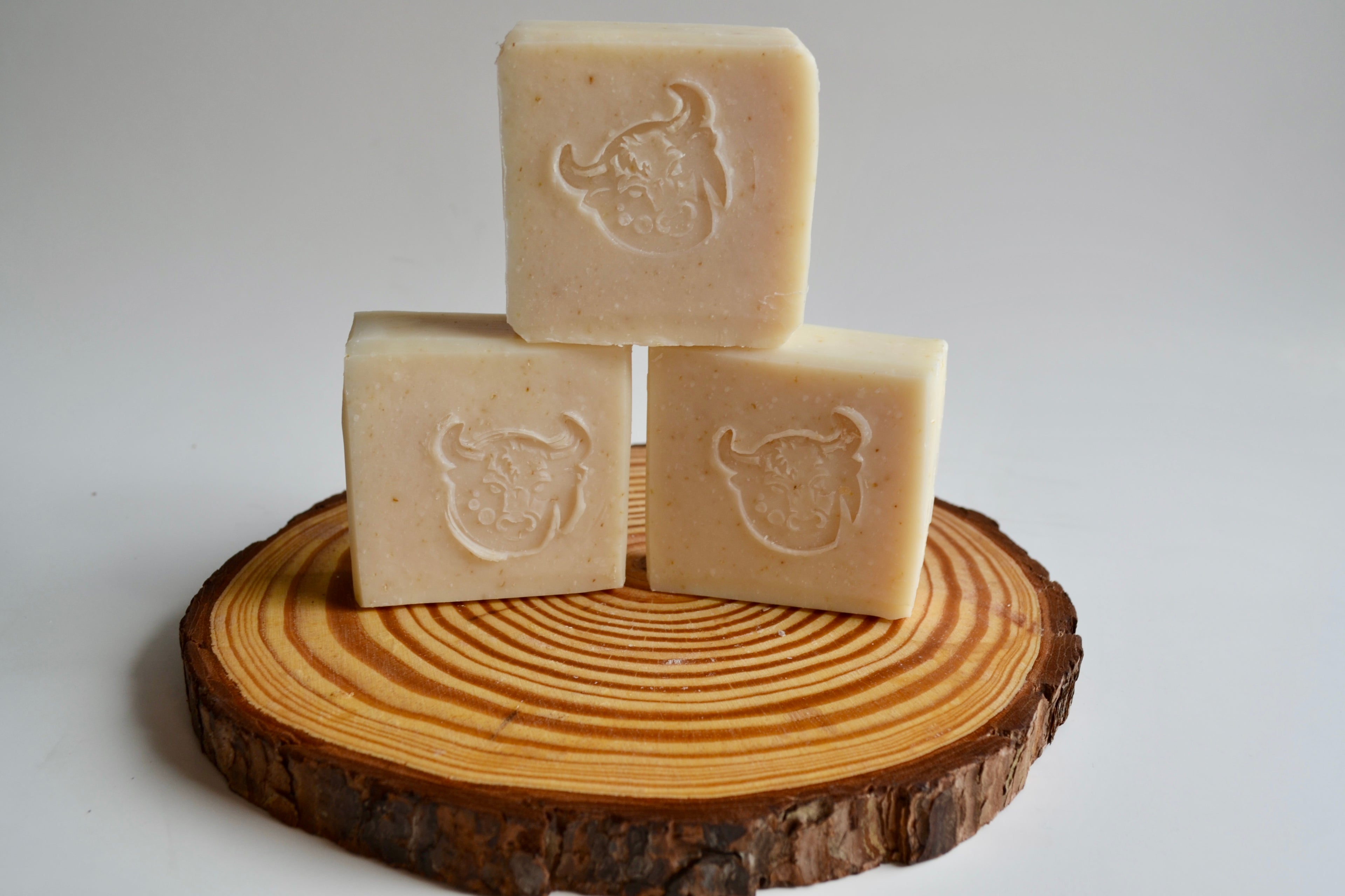 Three square soaps with a logo on a wooden block against a light background
