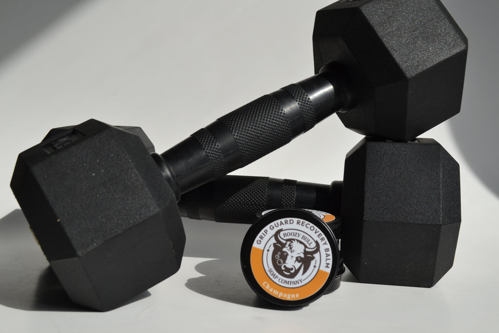 Pair of black hexagonal dumbbells with a weightlifting belt featuring a logo on a light gray background.