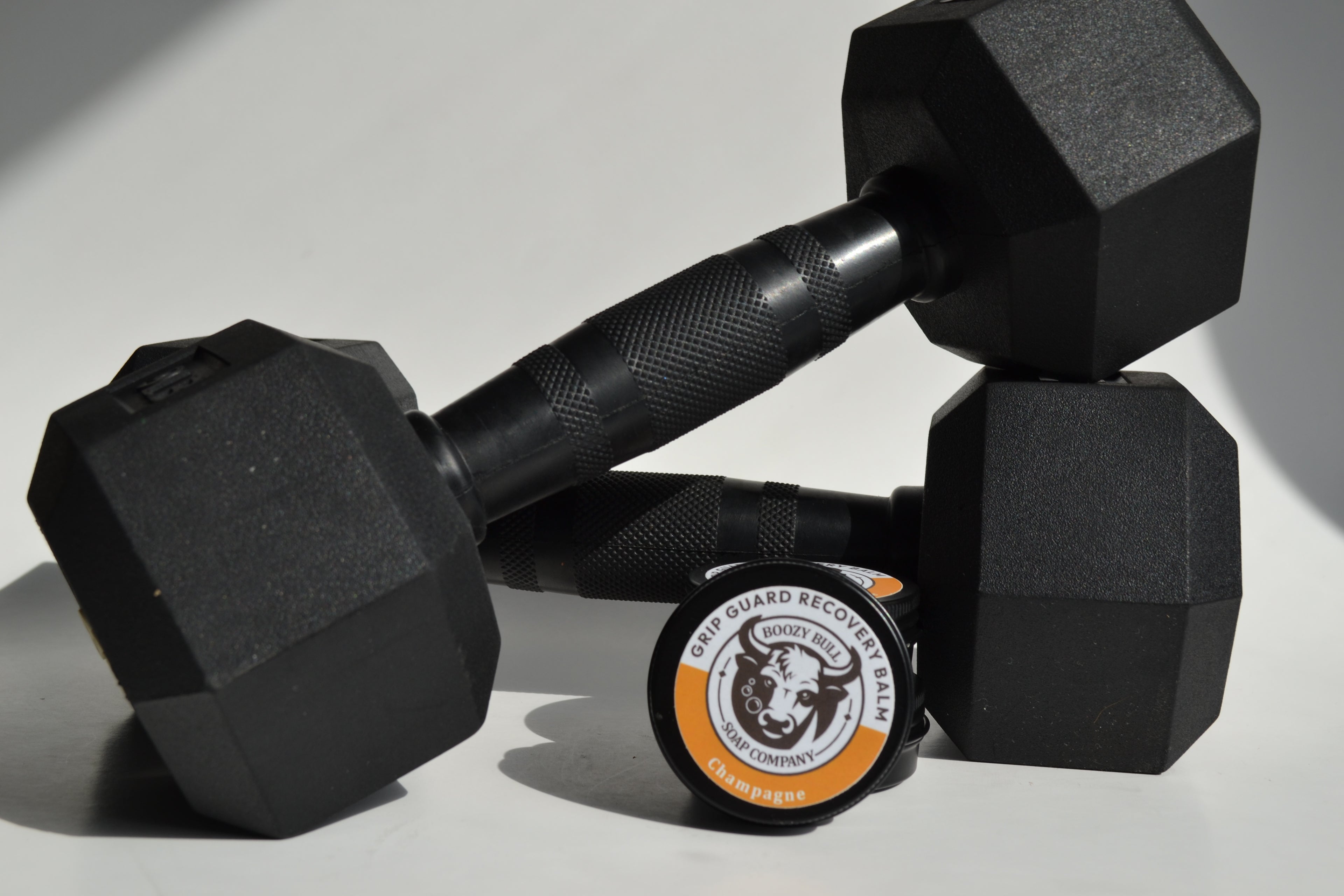 Pair of black hexagonal dumbbells with a weightlifting belt featuring a logo on a light gray background.