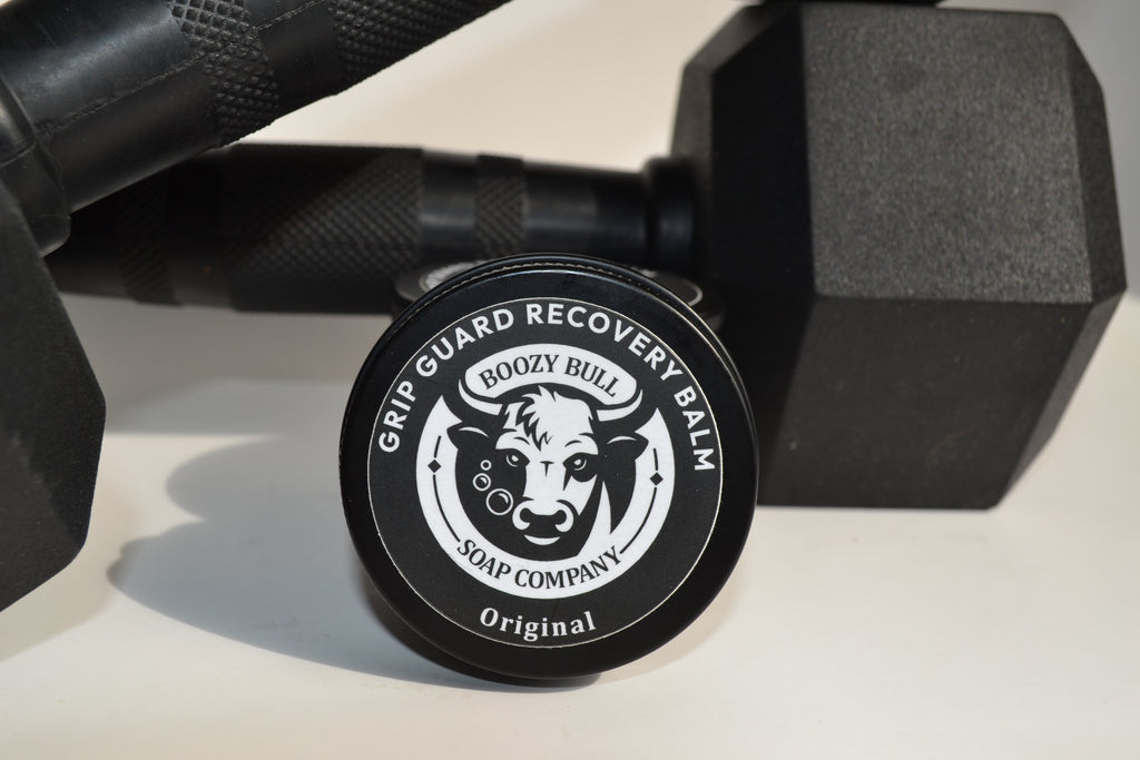 Grip Guard Recovery Balm container with 'Boozy Bull Soap Company' logo on a white surface with dumbbells.