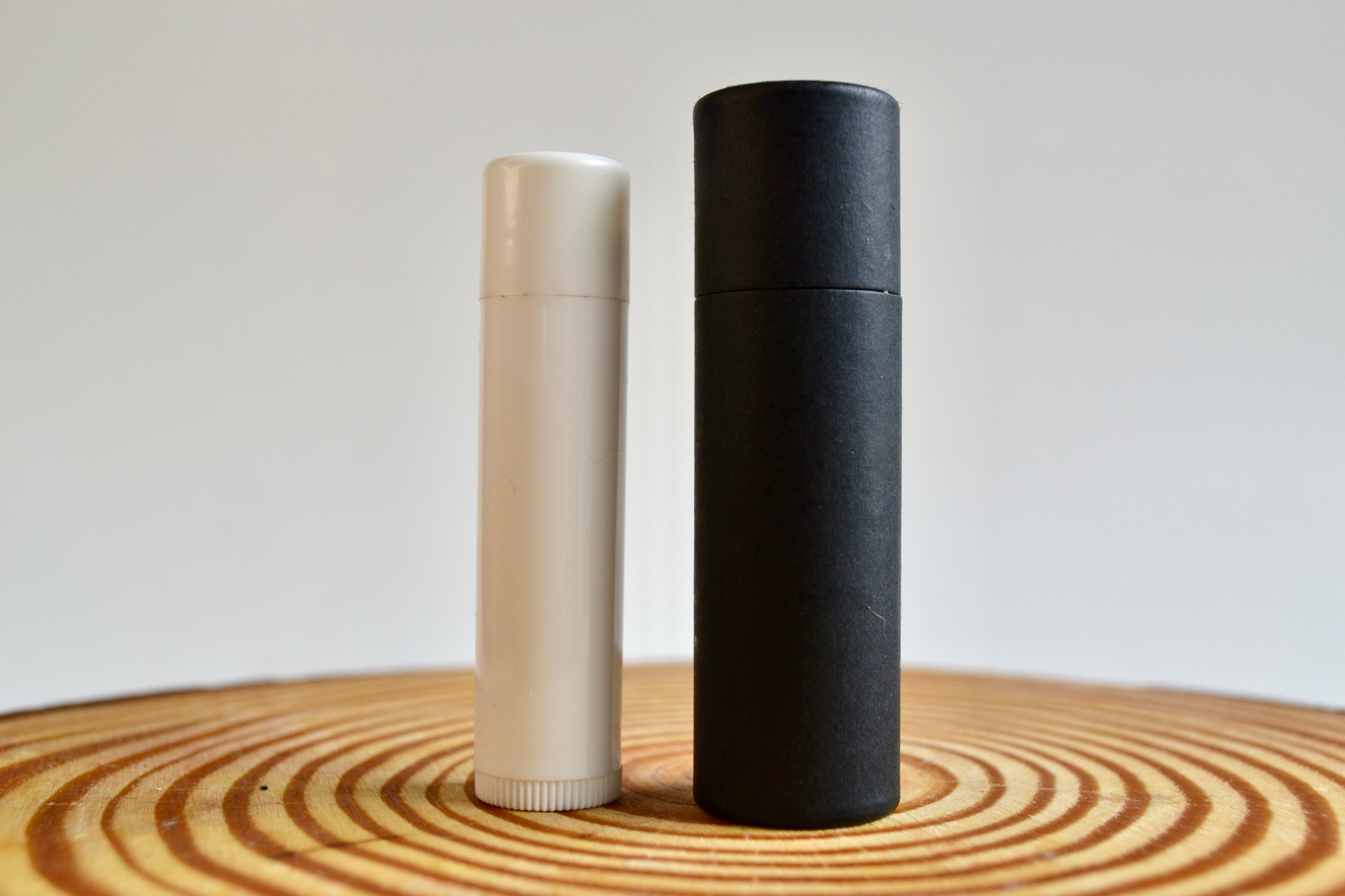 Black large cardboard lip balm tube compared to a white smaller ube.