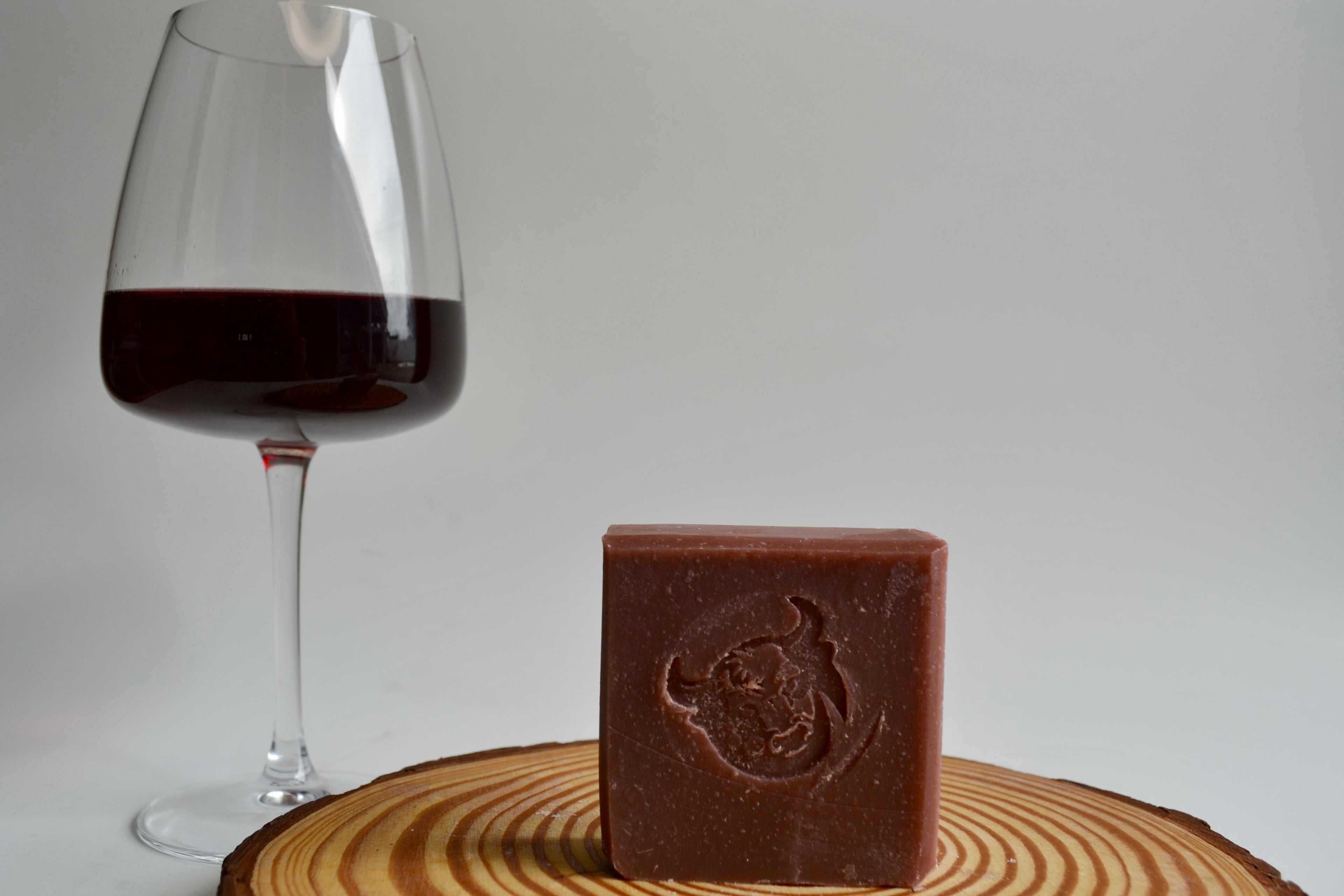 Bar of chocolate soap with a logo next to a glass of red wine on a wooden surface.