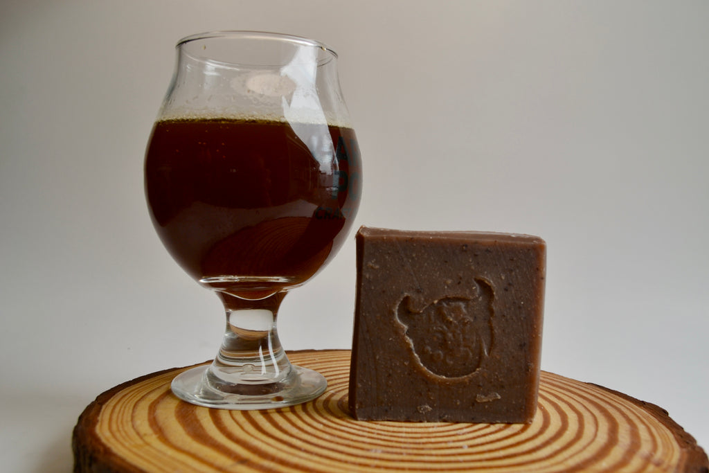 Glass of dark beer next to a bar of chocolate soap on a wooden surface