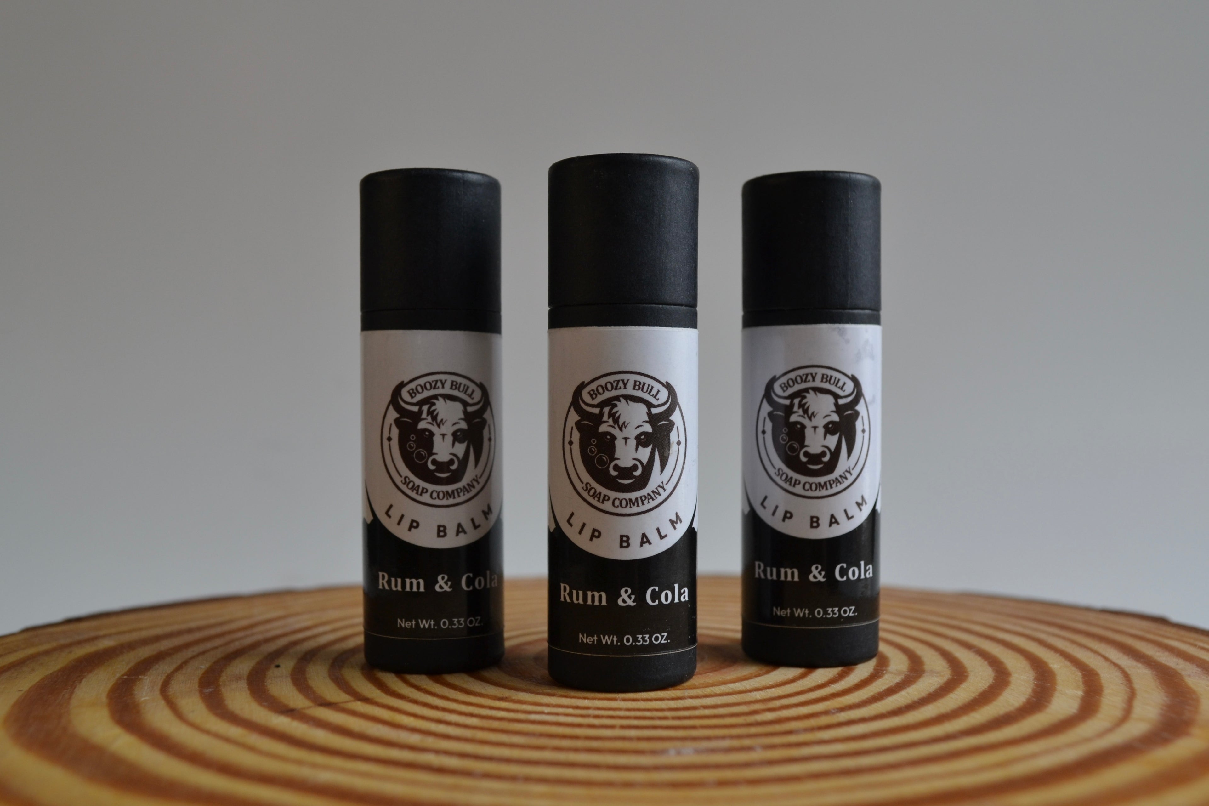 Three lip balm containers with black and white labels on a wooden surface.