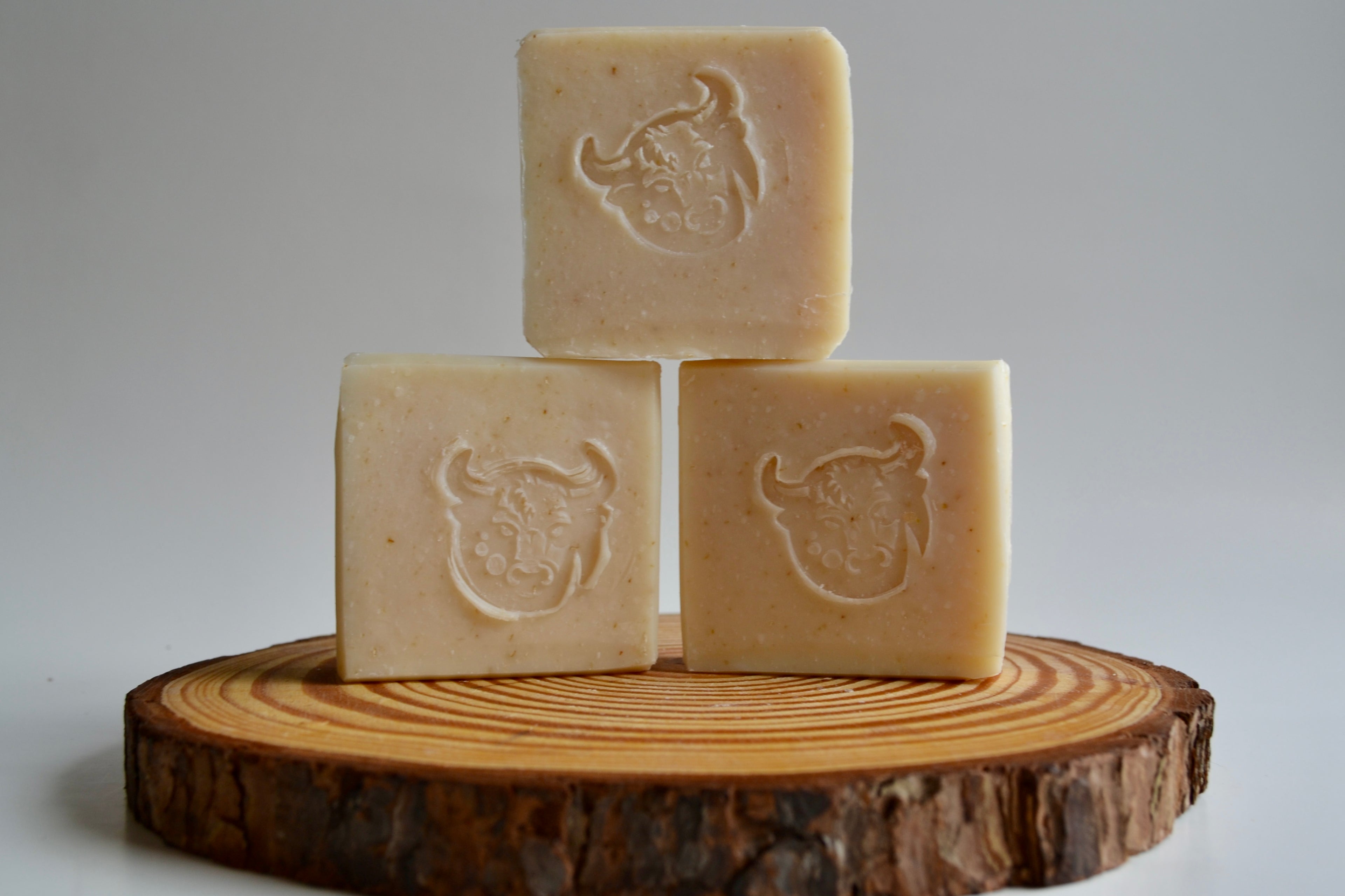 Three square bars of soap with embossed designs on a wooden stand against a gray background