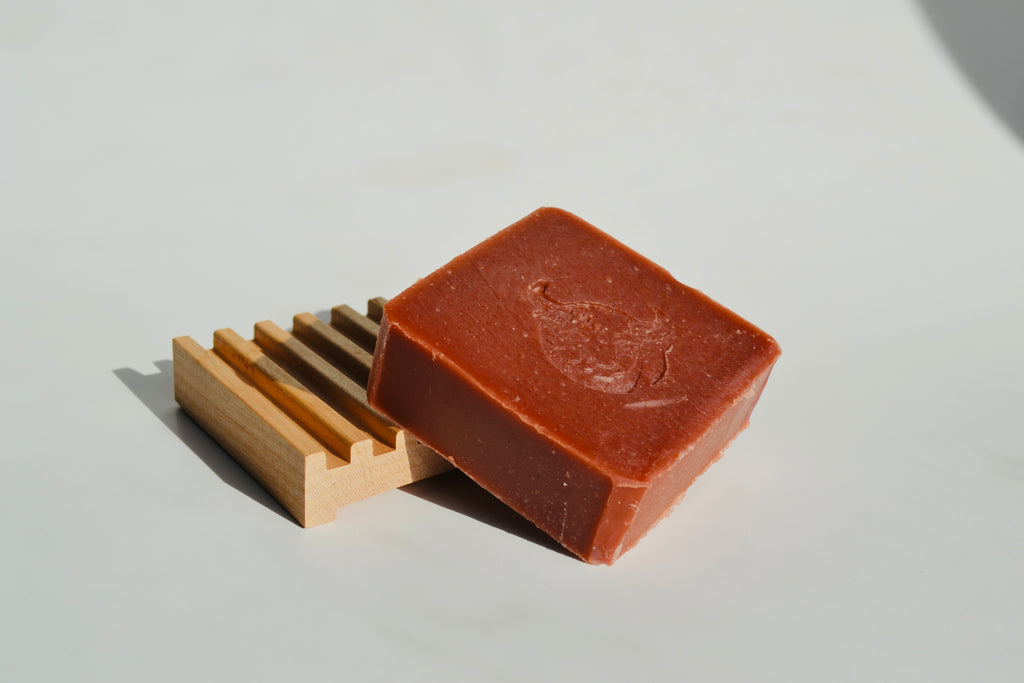 Bar of soap with a wooden soap dish on a light gray background