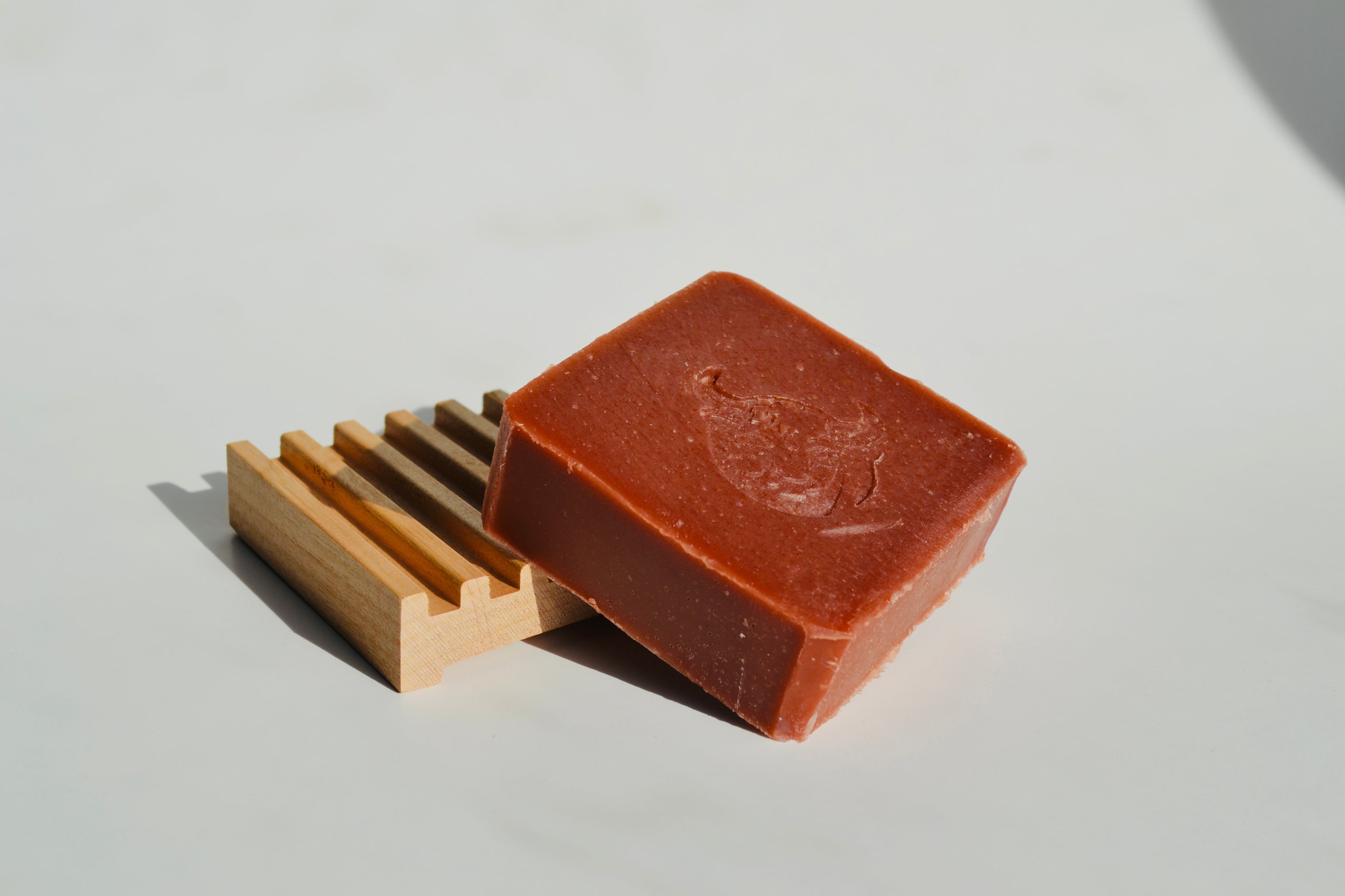Bar of soap with a wooden soap dish on a light gray background