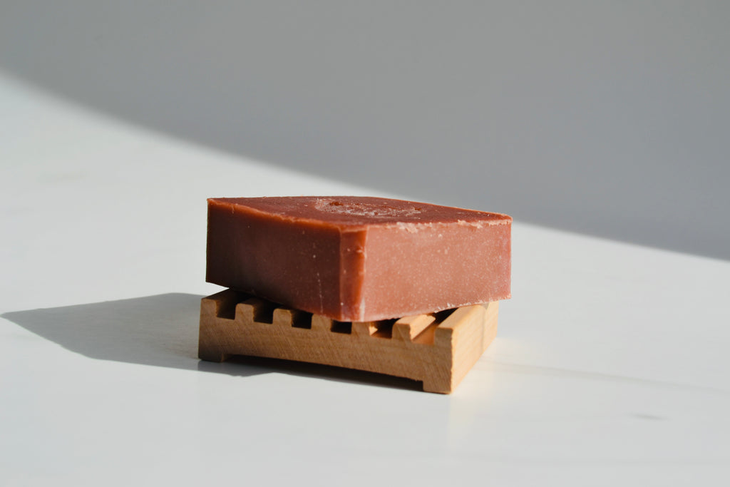 Bar of soap on a wooden soap dish with a neutral background