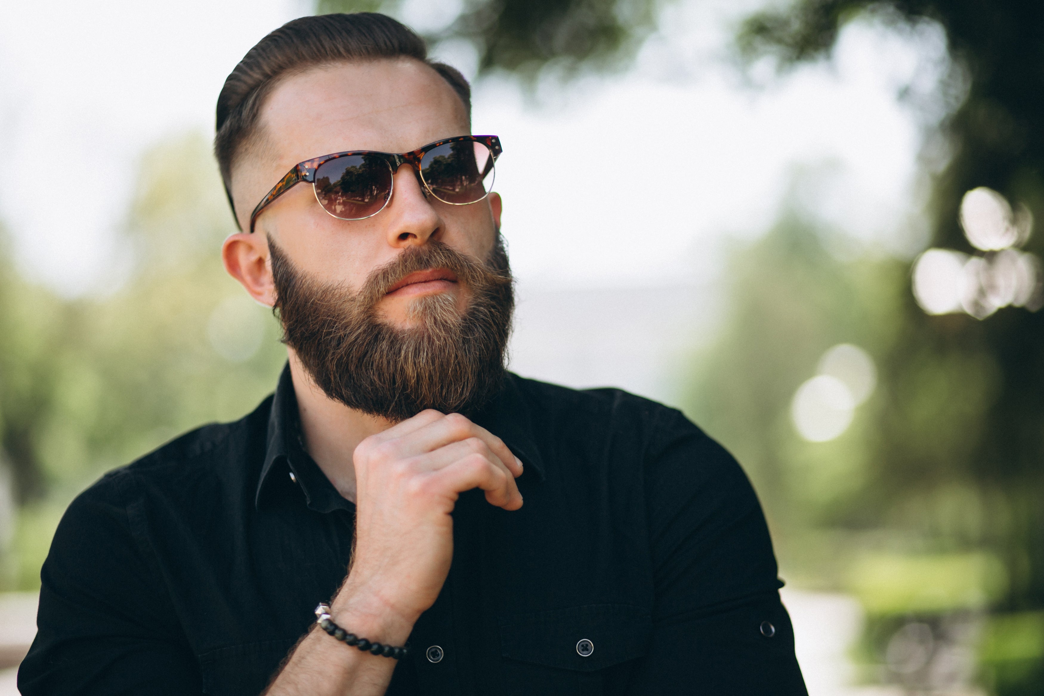 Man with a beard wearing sunglasses and a black shirt outdoors